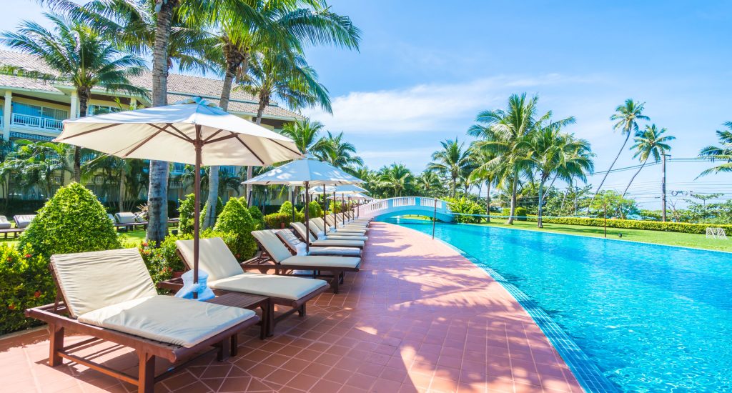 Beautiful luxury umbrella and chair around outdoor swimming pool in hotel and resort with coconut palm tree on blue sky - Boost up color Processing